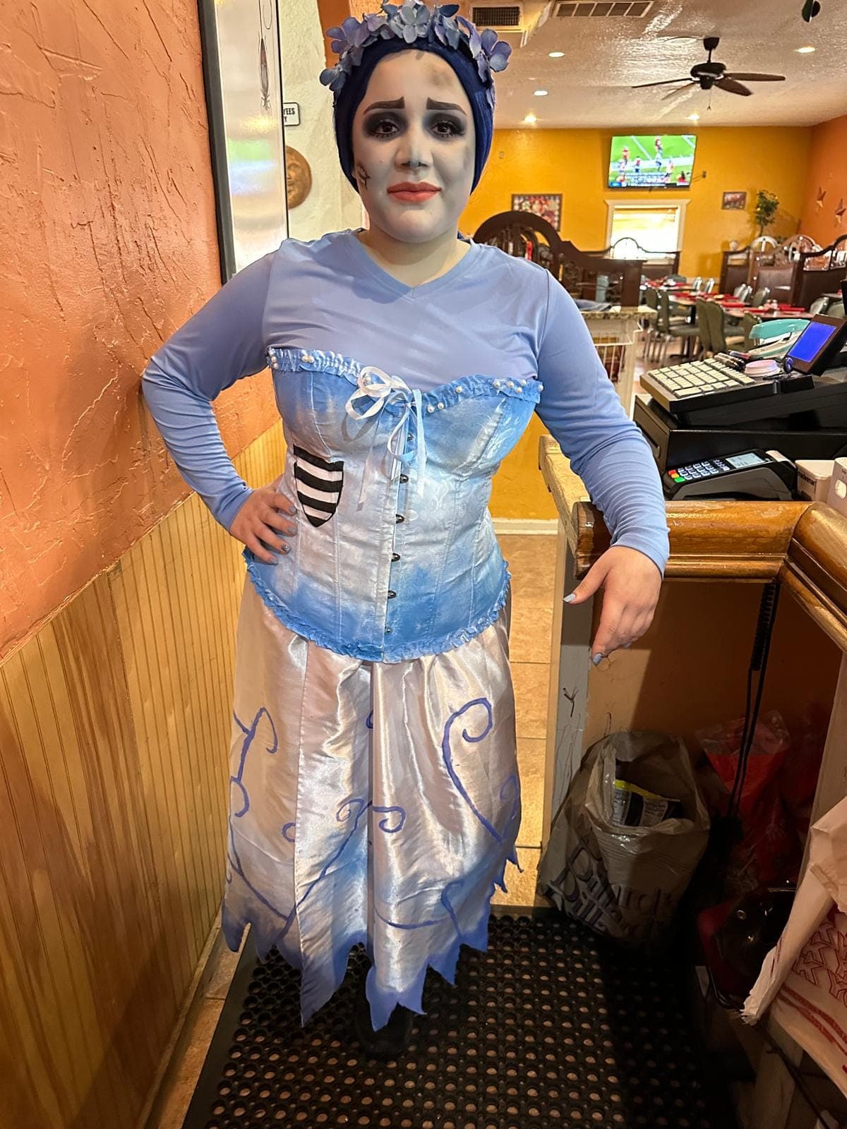 A member of staff in a blue corpse bride costume, posed by the register