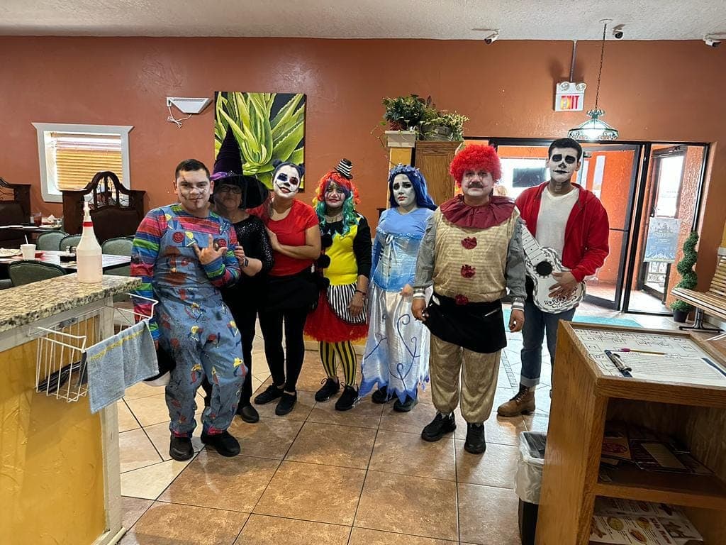 Seven staff at Abuelita Rosa's in Halloween costumes, posed together in the dining room