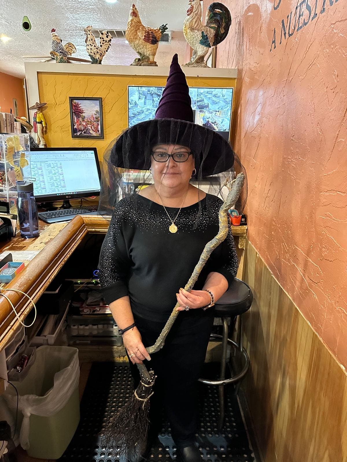 A member of staff in a witch hat holding a broom, behind the front counter