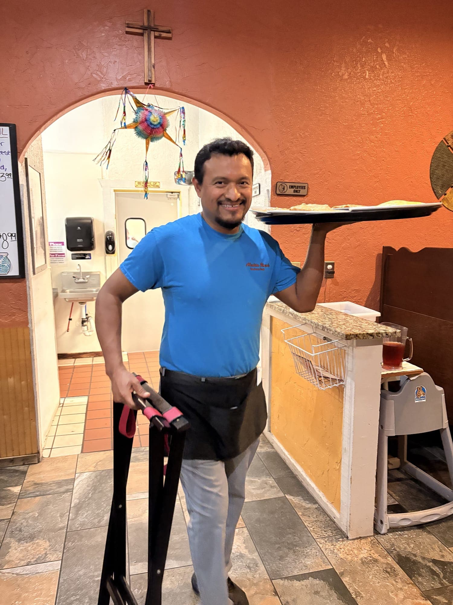 A server at Abuelita Rosa's carrying a tray of plates on one shoulder, smiling, under the arch in the dining room